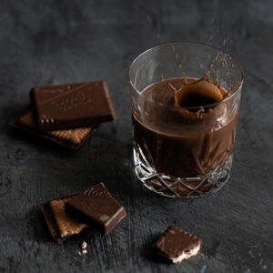 Cark chocolate flavored coffee in a glass next to bars of dark chocolate