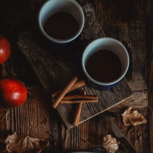 2 cups of French apple crumble cake flavored coffee next to two apples and 4 cinnamon sticks